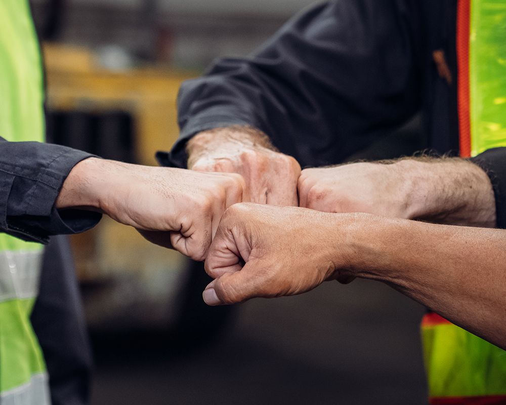 Varias manos de trabajadores chocándose después de hacer mantenimiento y reparación de motor eléctrico.